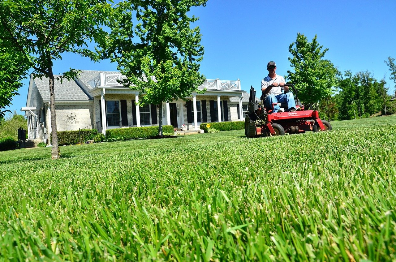 Person Riding a Lawnmower in Front of a House